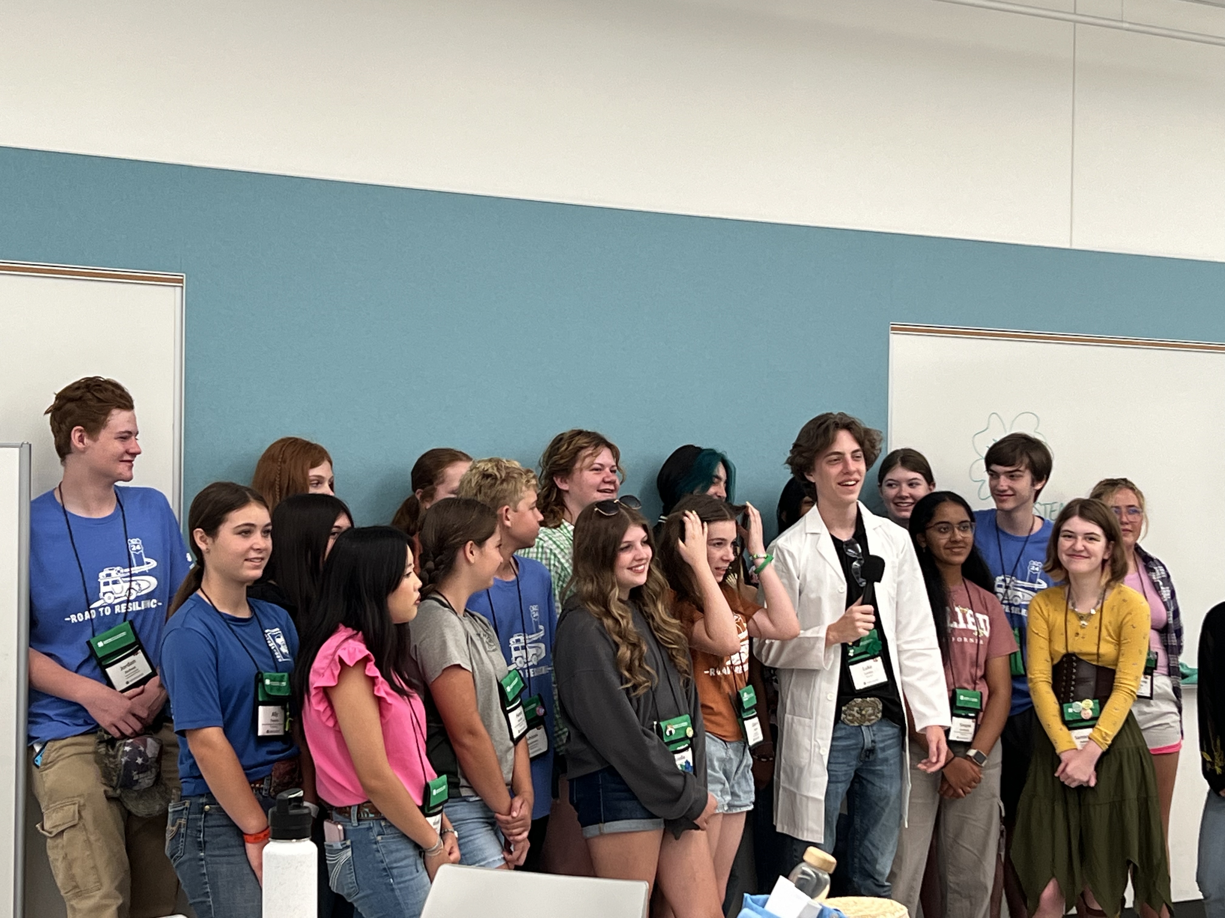 large group of youth standing around youth with lab coat holding a mic