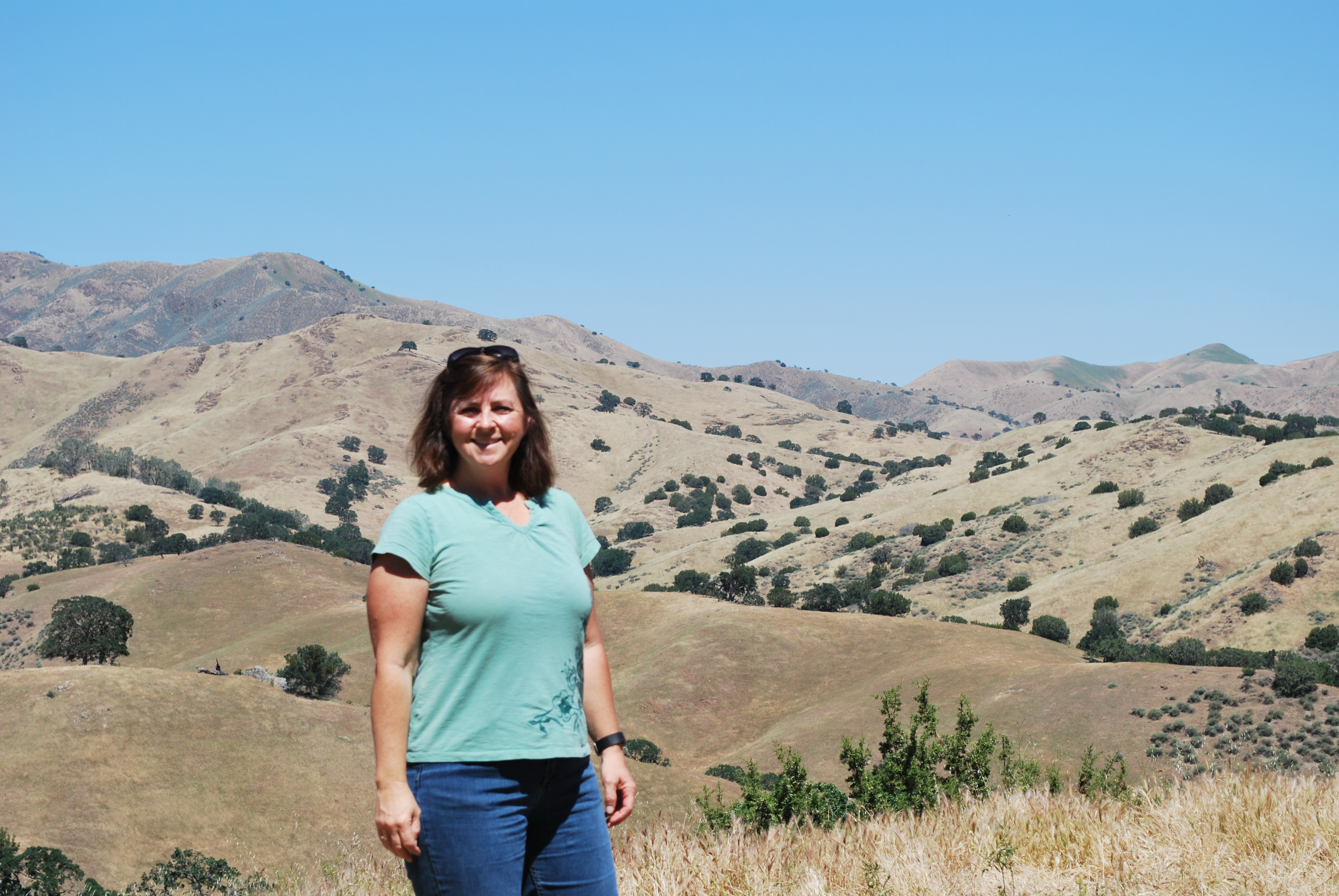 Theresa Becchetti standing on top of a hill with rolling rangelands behind her.