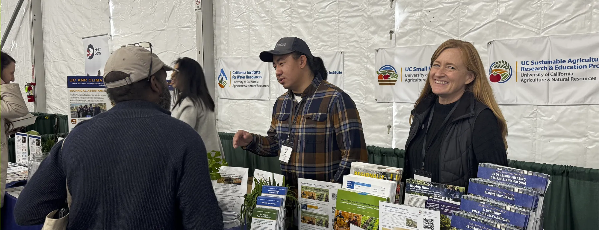 Two UC ANR representatives speak with an attendee during the EcoFarm 2026 conference.