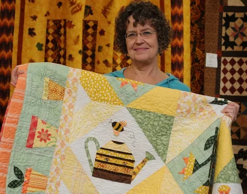 A HONEY BEE decorates a quilt at the 134th annual Dixon May Fair. Here Interior Living Showcase superintendent Debee Lamont gets ready to hang the quilt. It's the work of Shirley Geertson of Vacaville. (Photo by Kathy Keatley Garvey)