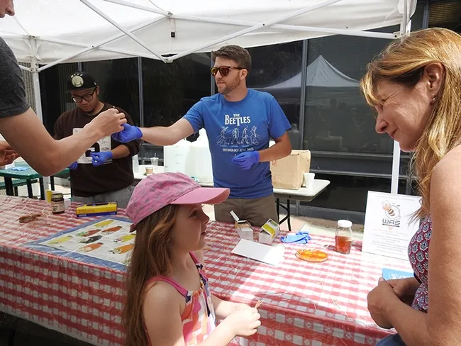 Graduate student Jackson Audley of the Steve Seybold lab hands a honey-coated toothpick to a participant. At far left is graduate student Wei Lin of the Brian Johnson lab. (Photo by Kathy Keatley Garvey)