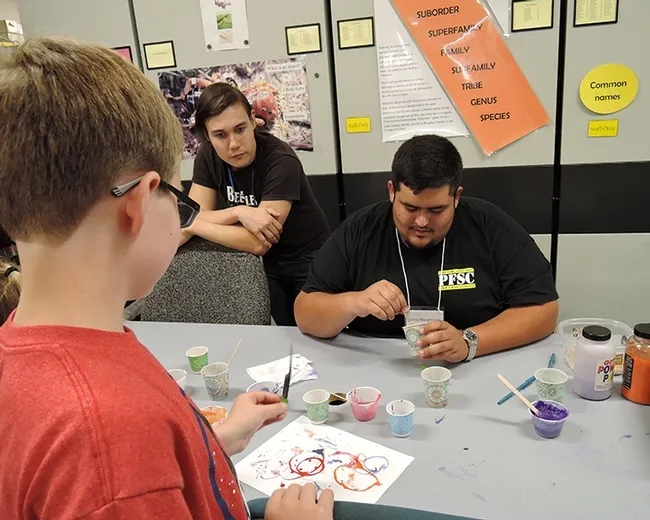 UC Davis graduate student Alexander Dedman (left), who studies with major professor Robert Kimsey, watches as NAFEA member Greg Nigoghosian of Purdue dips a maggot into its "bath": non-toxic, water-based paint. (Photo by Kathy Keatley Garvey)