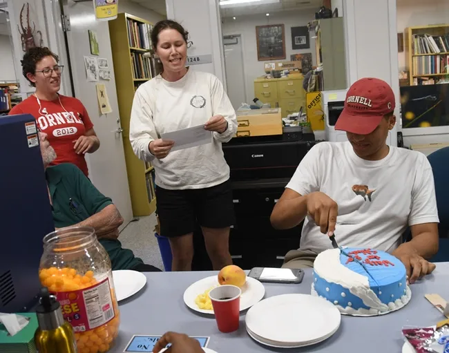 Cornell alumni Emily Bick (left) and Tabatha Yang serenade Noah Crockette as he cuts his cake at the Bohart Museum's going-away party. (Photo by Kathy Keatley Garvey)
