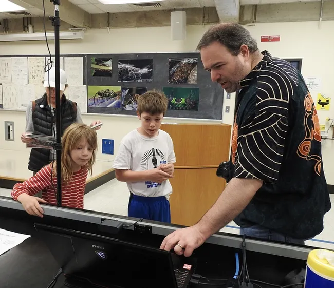 UC Davis medical entomologist Geoffrey Attardo shows Sebastian and Kamila Ehrlich examples of what insects they might want to see in virtual reality. In back is their mother, Carollina Ehrlich. (Photo by Kathy Keatley Garvey)