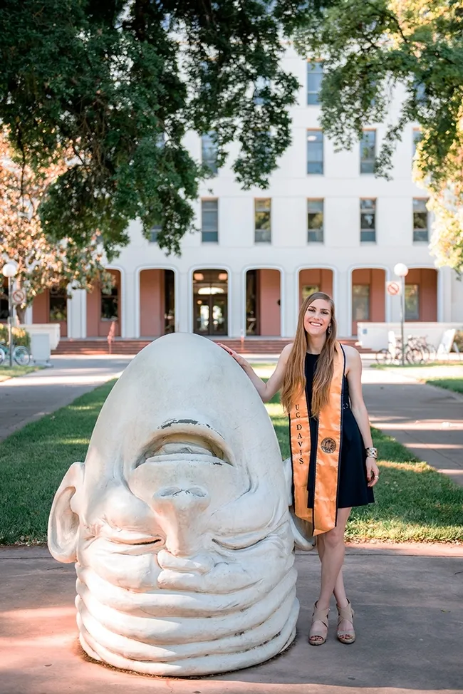 UC Davis fourth-year student Jessica Macaluso stands next to artist Robert Arneson's egghead sculpture in front of Mrak Hall. She will receive her bachelor's degree in psychology this fall.