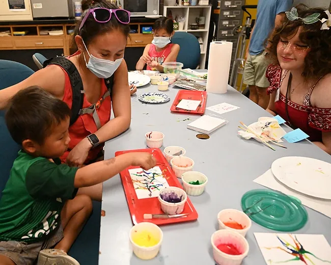 Isaiah Hu, 4, of Davis, works on his Maggot Art creation, while his mother, Lisa Hu (next to him) and Bohart Museum associate Kat Taylor, a UC Davis entomology major, watch. Lisa is a 2011 graduate (DVM) of the UC Davis School of Veterinary Medicine. (Photo by Kathy Keatley Garvey)