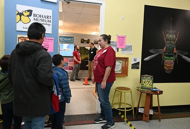 Bohart associate and entomologist, Nazzy Pakpour, PhD, author of "Please Don't Bite Me: Insects that Buzz, Bite and Sting," greets guests at the Bohart Museum. In back are Bohart director Jason Bond (right) conversing with Brennen Dyer, collections manager. (Photo by Kathy Keatley Garvey)