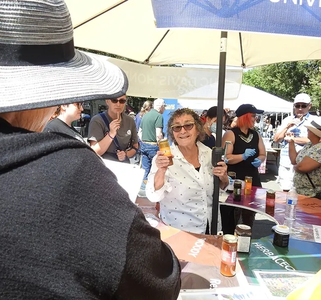 "Queen bee" Amina Harris, retired director of the UC Davis Honey and Pollination Center that she founded in 2012, also co-founded the California Honey Festival in 2017. In this archived photo from last year, she offers attendees a taste of honey. (Photo by Kathy Keatley Garvey)