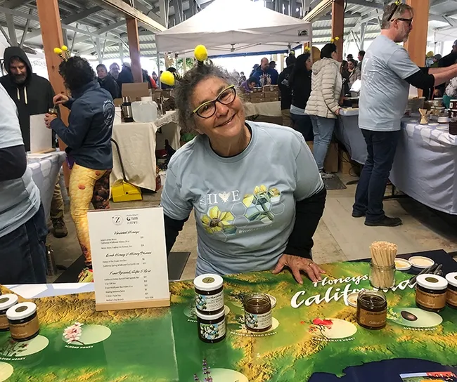 Amina Harris, retired founding director of the UC Davis Honey and Pollination Center and now the "queen bee" of her family's Woodland-based Z Food Specialty and The HIVE, offers attendees a taste of honey. She and the City of Woodland co-founded the California Honey Festival in 2017. (Photo by Kathy Keatley Garvey)