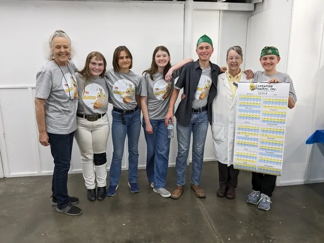 2 adults stand with 5 youth holding a large calendar poster
