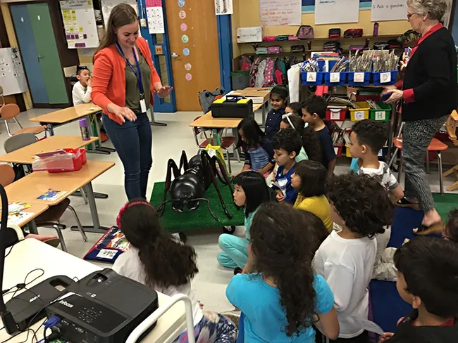 Nicole Keough leads an outreach event. As an undergraduate student, she was volunteering at a public ESL (English-as-second language) elementary school, teaching first grade students about ant physiology and anatomy. Note the large ant in front of her.