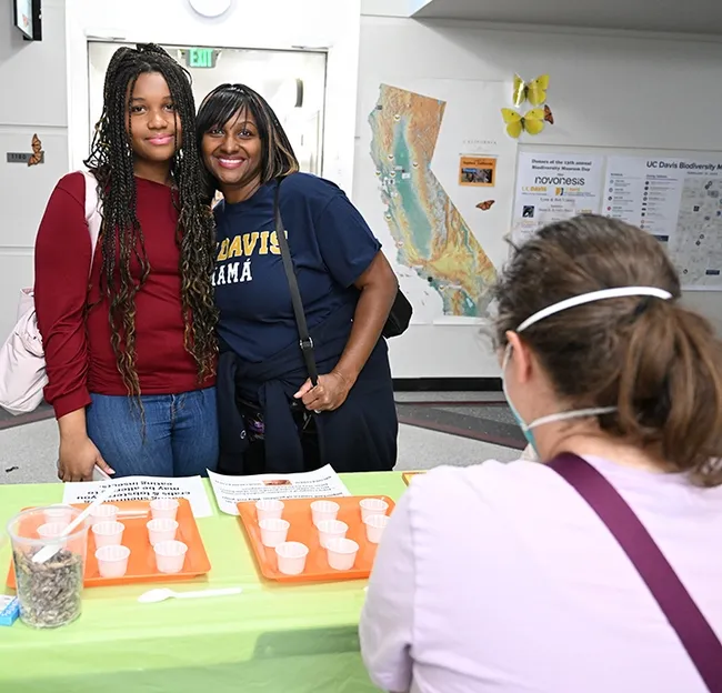 UC Davis student Nia Rhodes, an atmospheric science major, stopped by the cricket booth with her mother, Elizabeth Rhodes of Los Angeles, who is wearing a "UC Davis Mama" shirt. It was Davis Parent and Family Weekend. In the foreground is Tabatha Yang, the Bohart Museum's education and outreach coordinator. (Photo by Kathy Keatley Garvey)