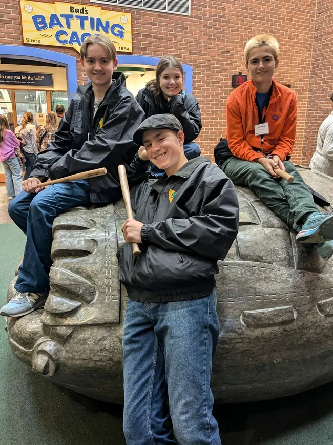 4 youth posing with Little Slugger baseball bats, sitting on a baseball mitt sculpture
