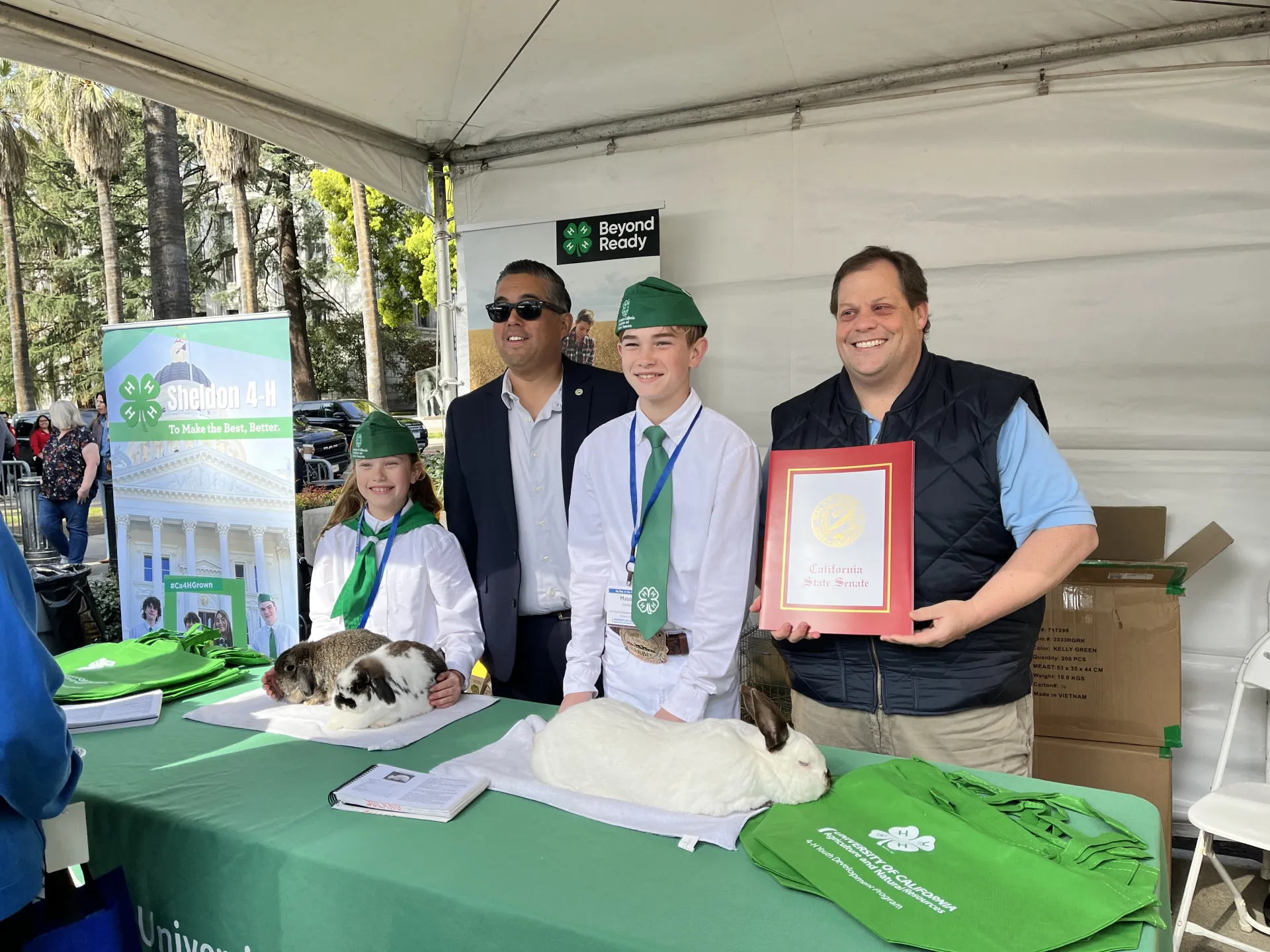 Two men stand with two 4-H members wearing their green and white uniforms