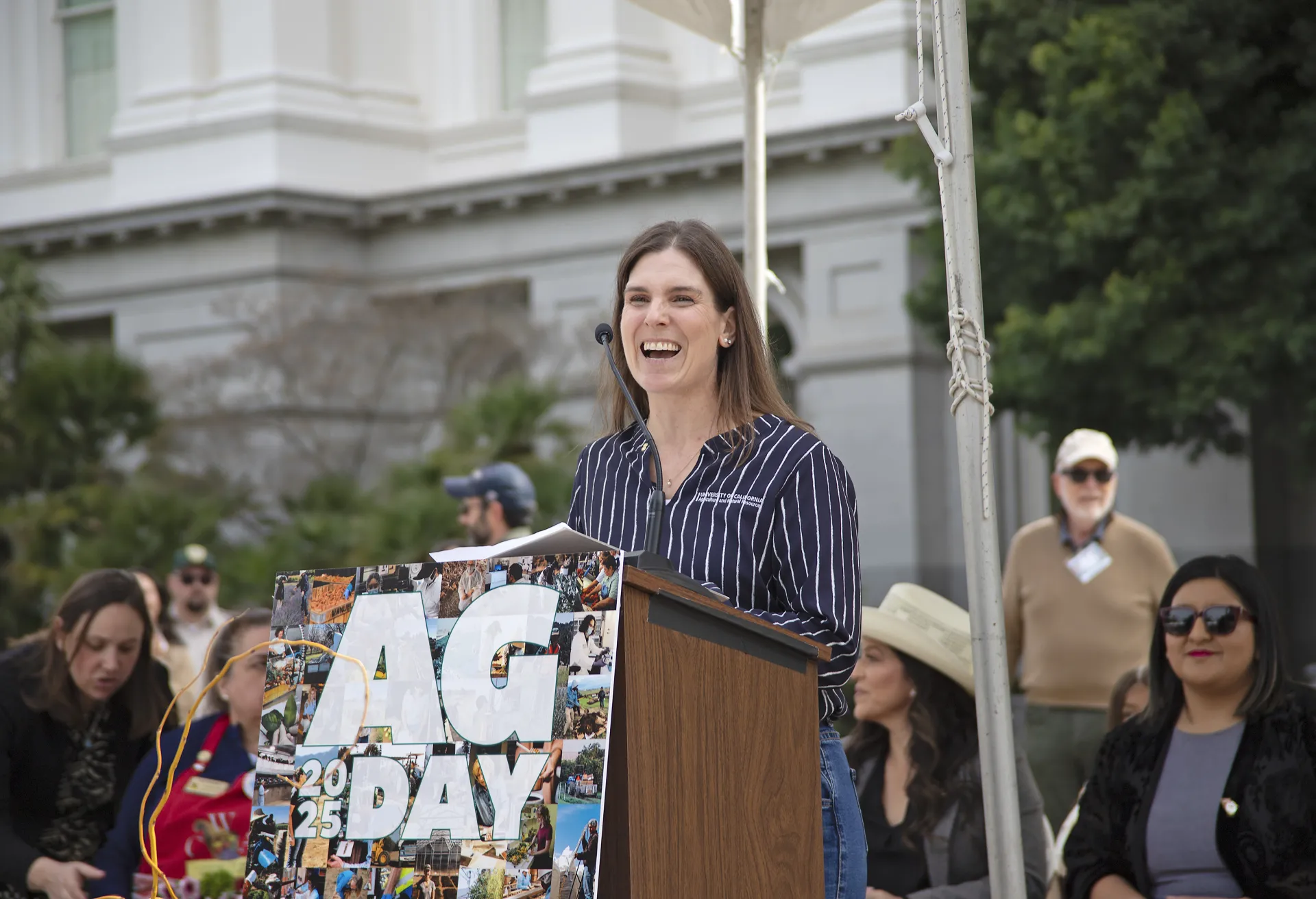 Betsy Karle, laughing, speaks at a lectern on stage