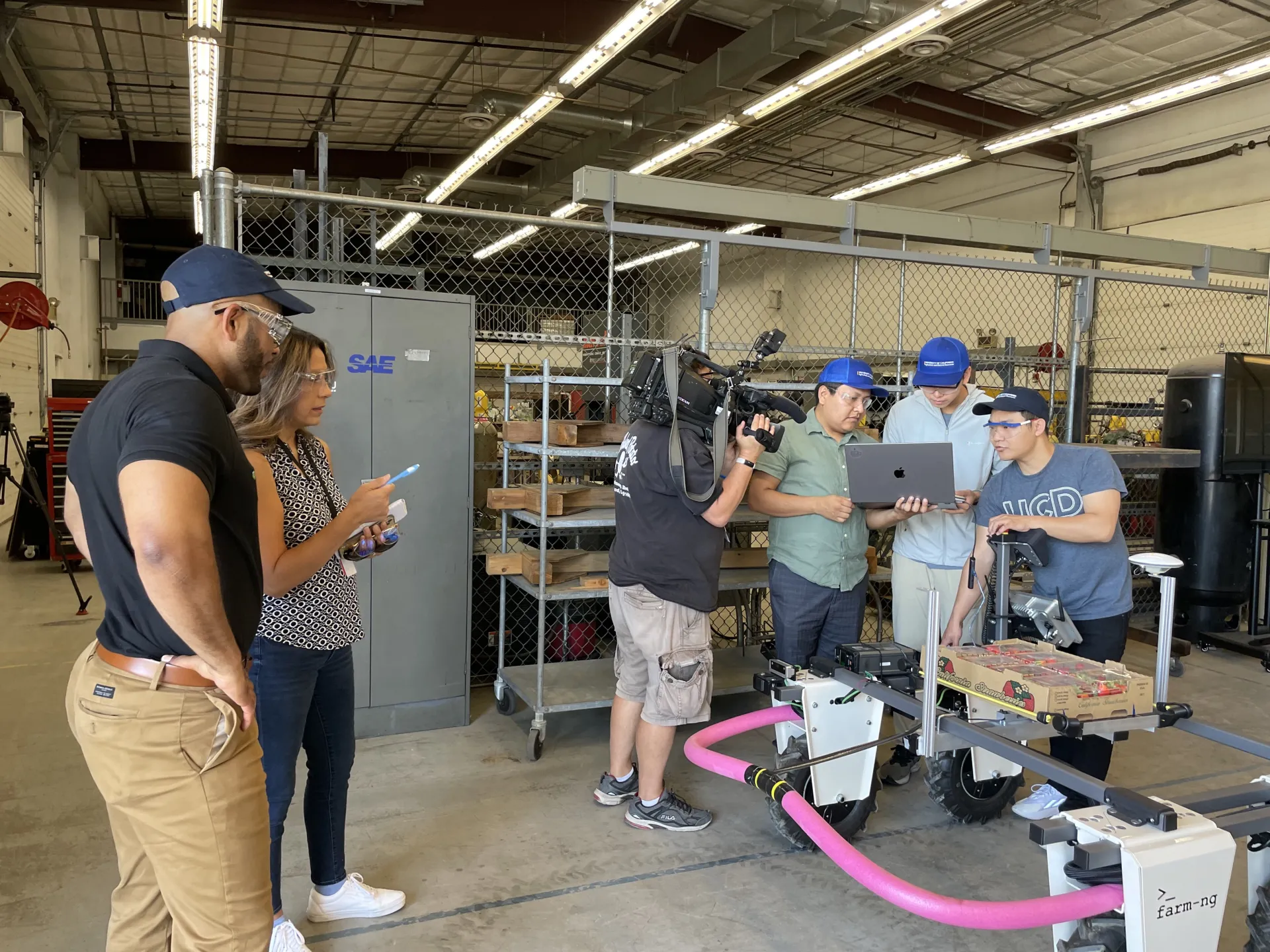 A cameraman points a TV camera at three guys looking at a laptop to maneuver a robot