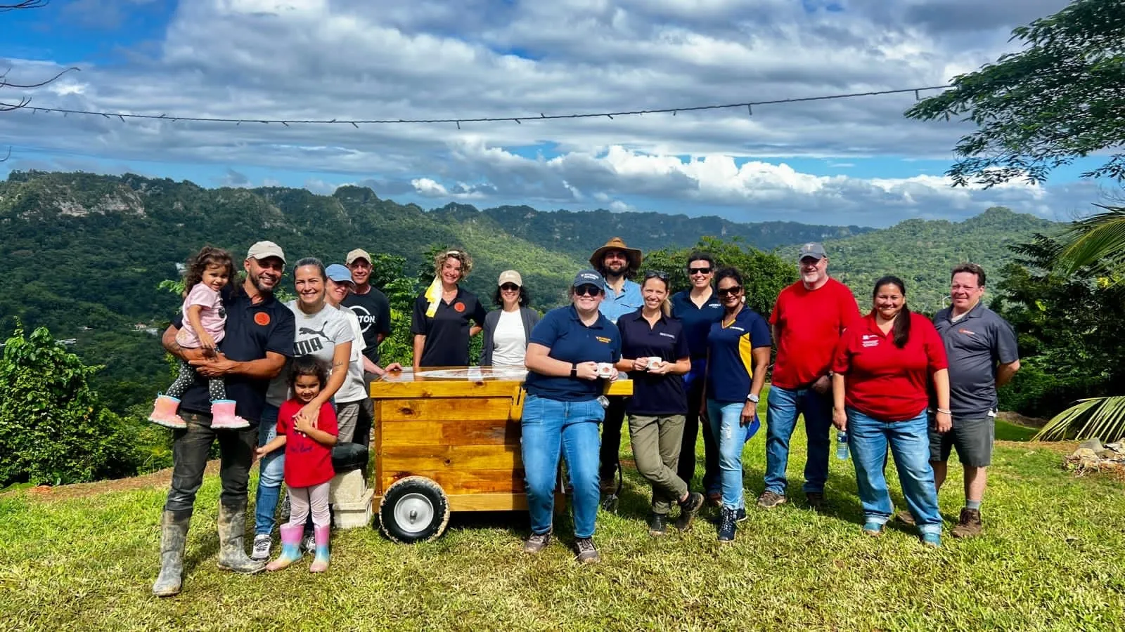 A group of people standing with a coffee cart with a lush mountain range in the background