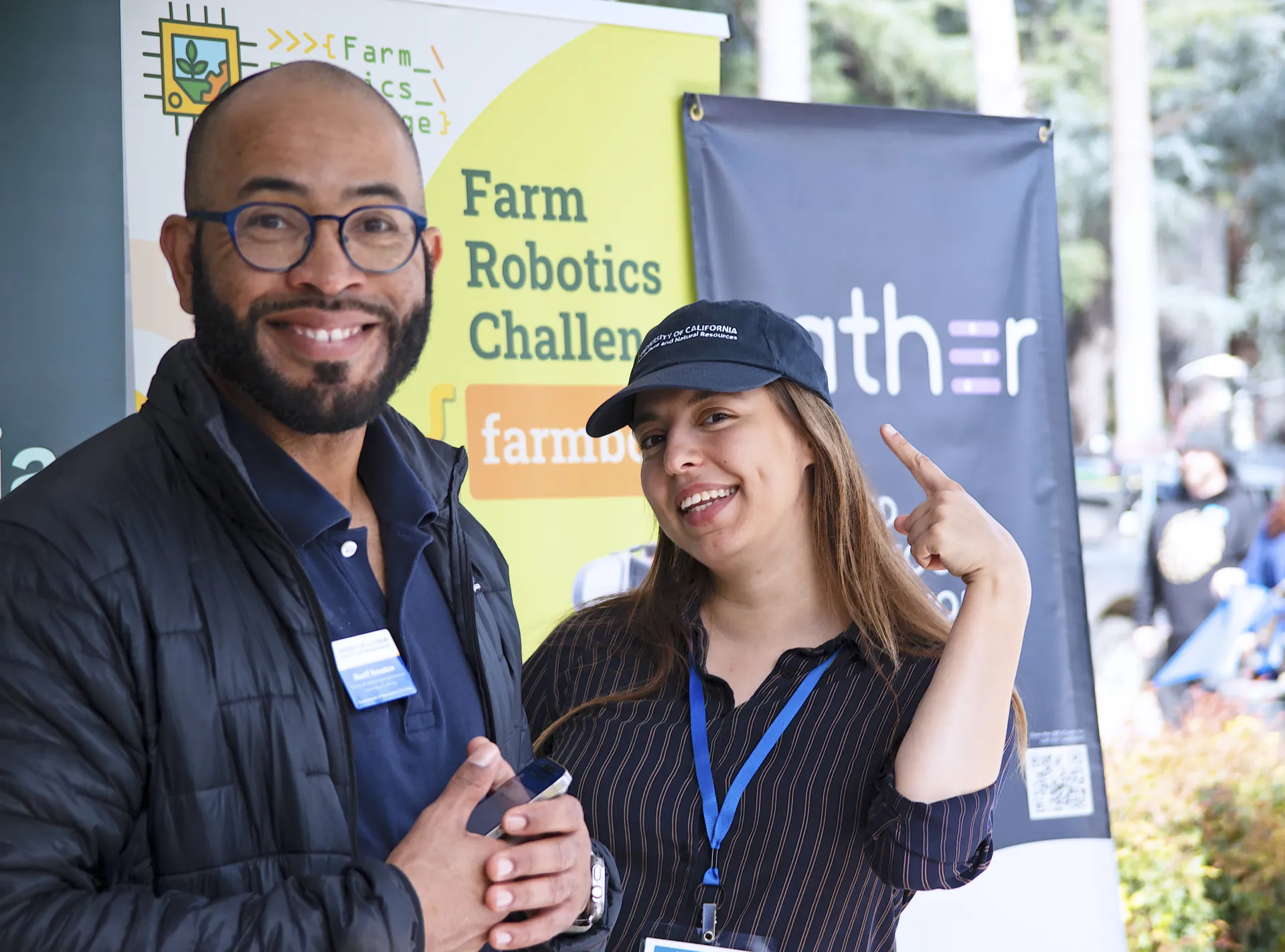 Hanif Houston and Lucie Cahierre pose in front of the Farm Robotics Challenge sign. Lucie points to the sign. 