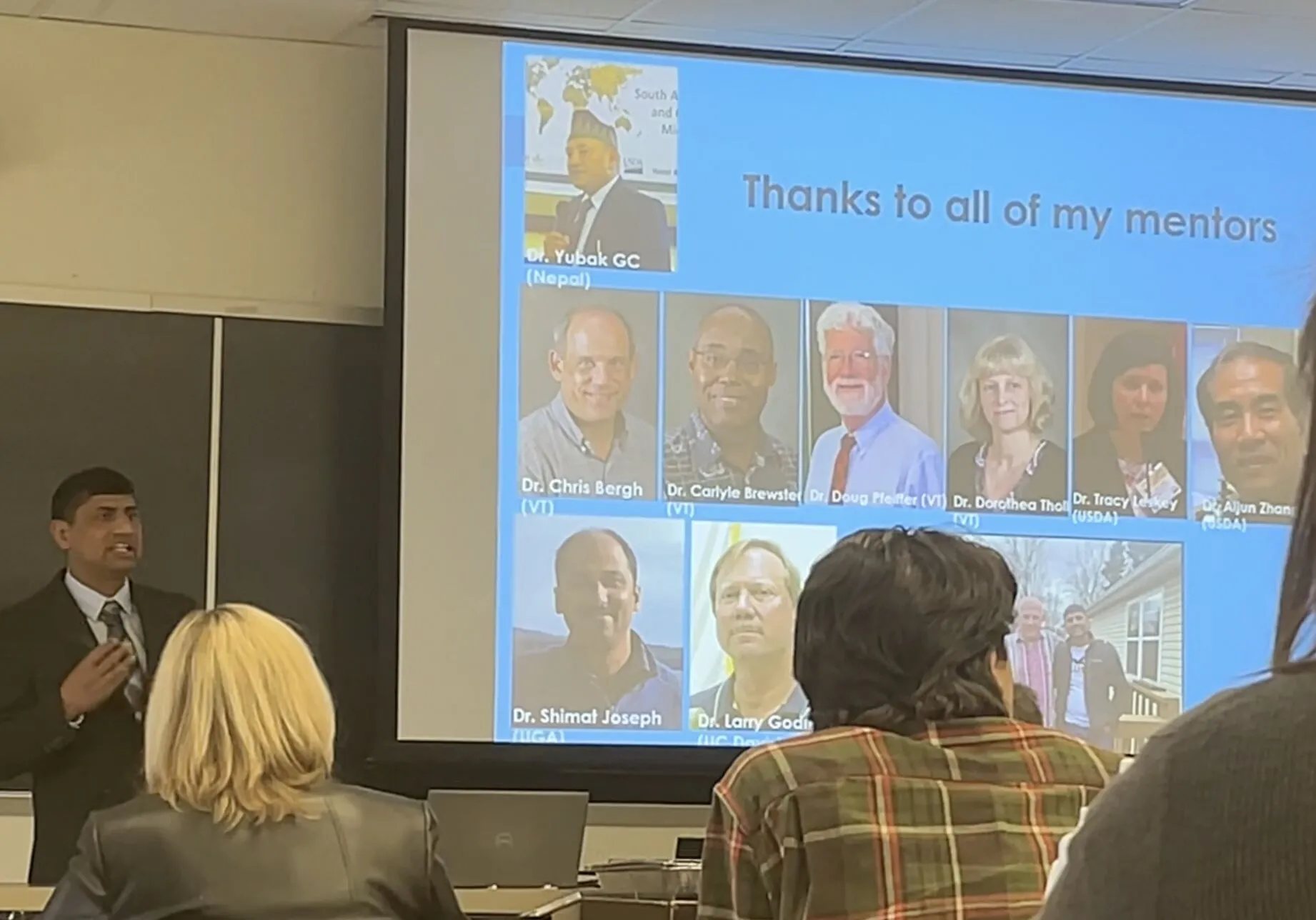Jhalendra Rijal, standing next to a PowerPoint slide that reads, "Thanks to all of my mentors," speaks to people in a classrooom.