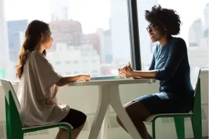 Two employees sit across from each other at a table, engaged in conversation.