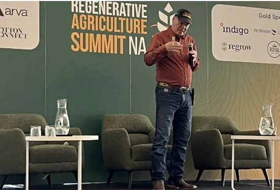 Man in jeans and a ballcap speaks in front of a Regenerative Agriculture Summit, North America backdrop.