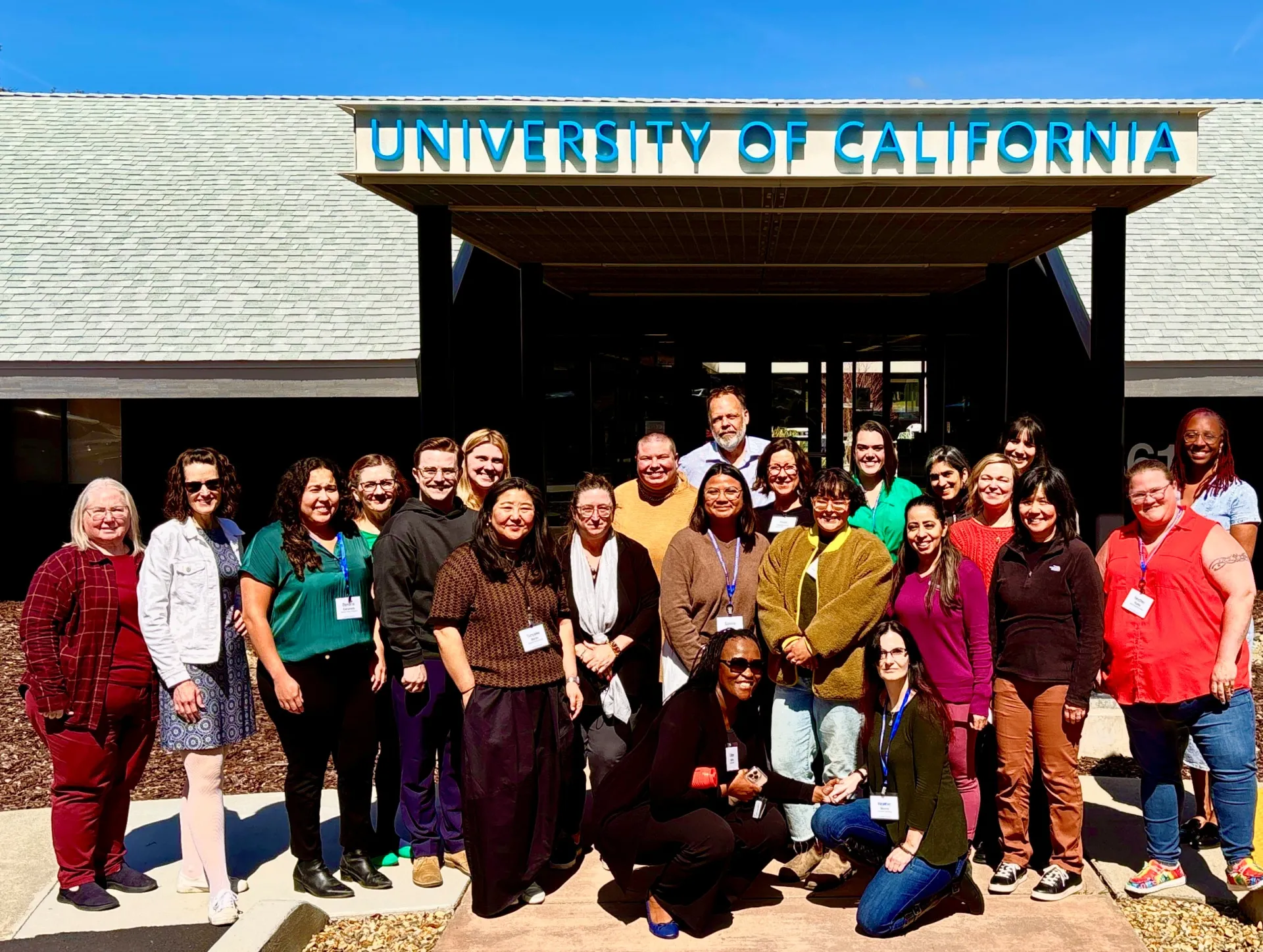 a group of 25 people in front of a Univ of California sign