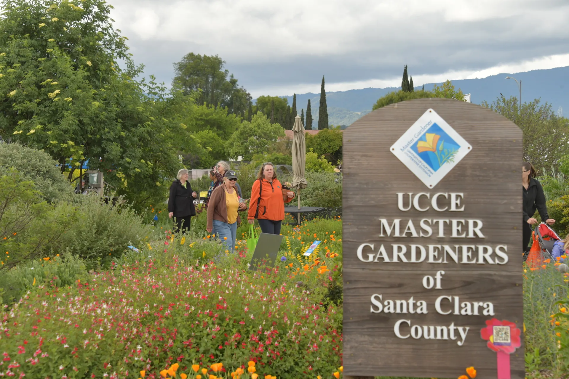 Five people walk among flowering plants. Sign in foreground reads: UCCE Master Gardeners of Santa Clara County