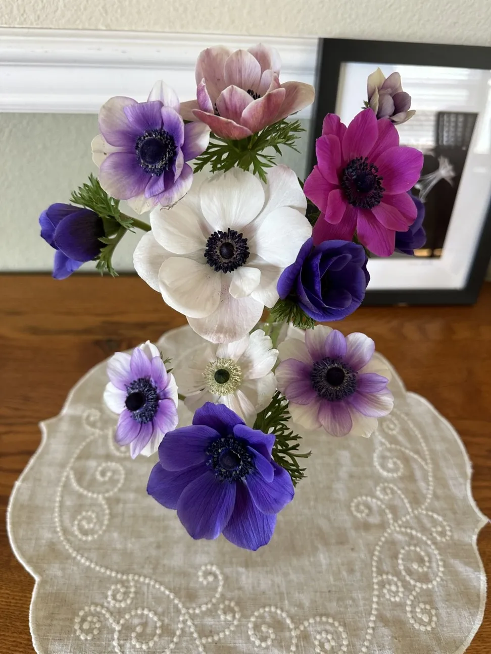 white, purple and blue anemone flowers adorn a table with a doily