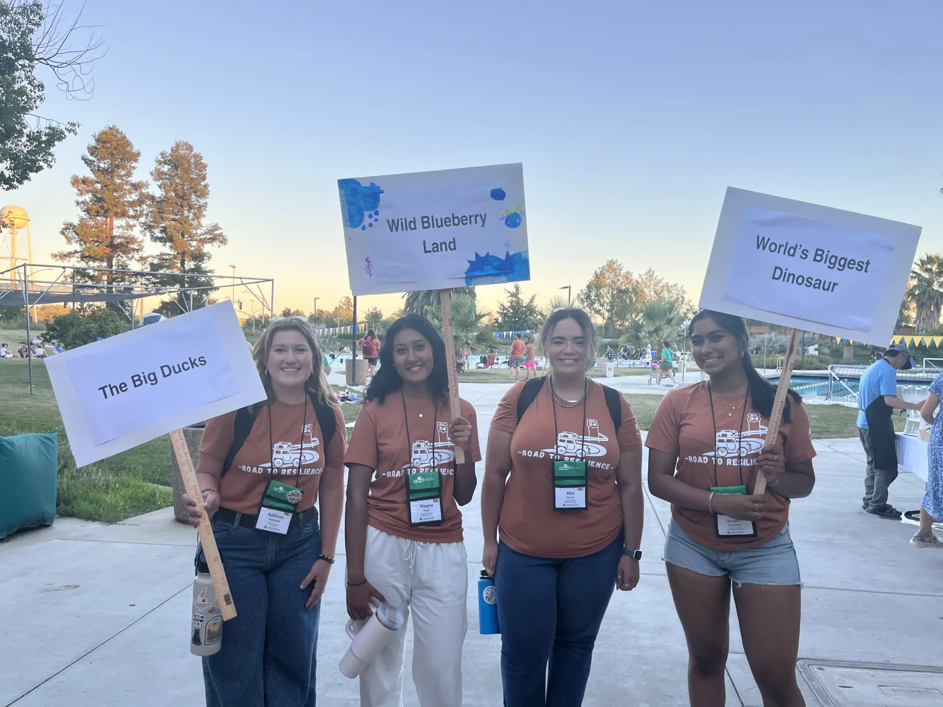 4 Program Assistants posing with their group names on signs on sticks