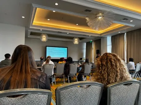People sit in chairs in a conference room listening to a speaker