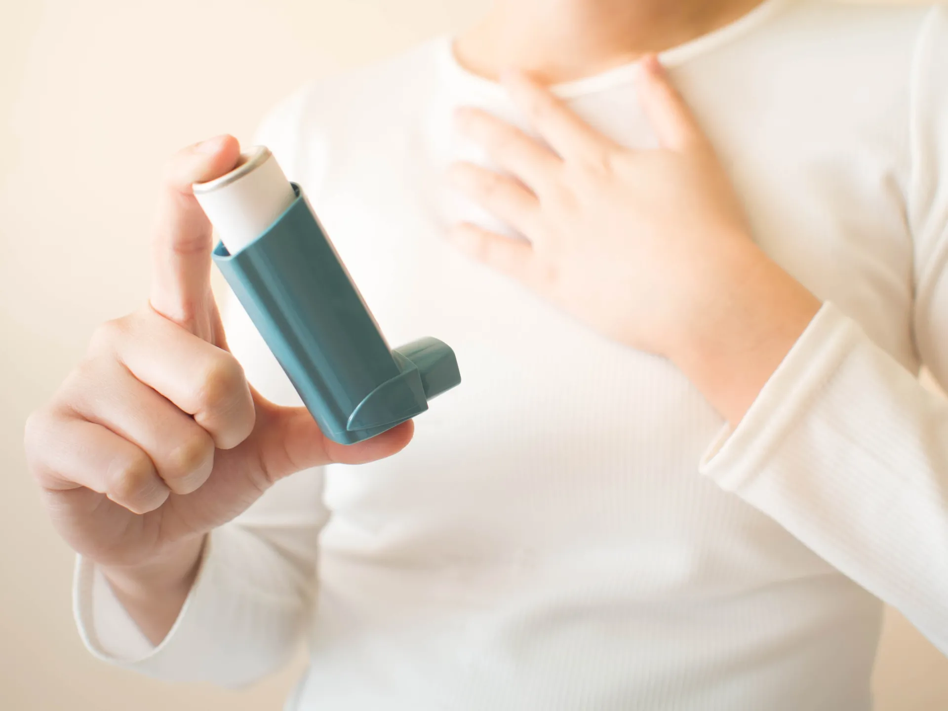 A person holding an inhaler in one hand and clenching their chest with the other.
