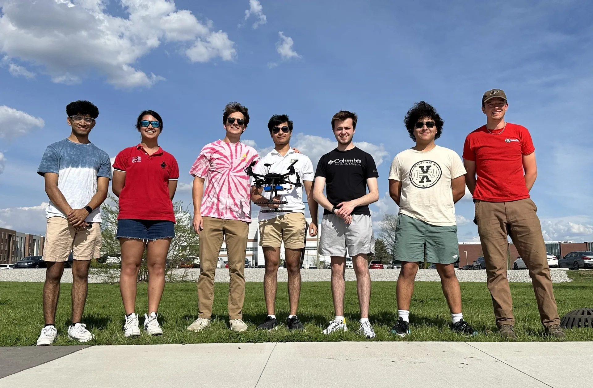Seven people stand in a line on grass, the guy in center holds a small drone.