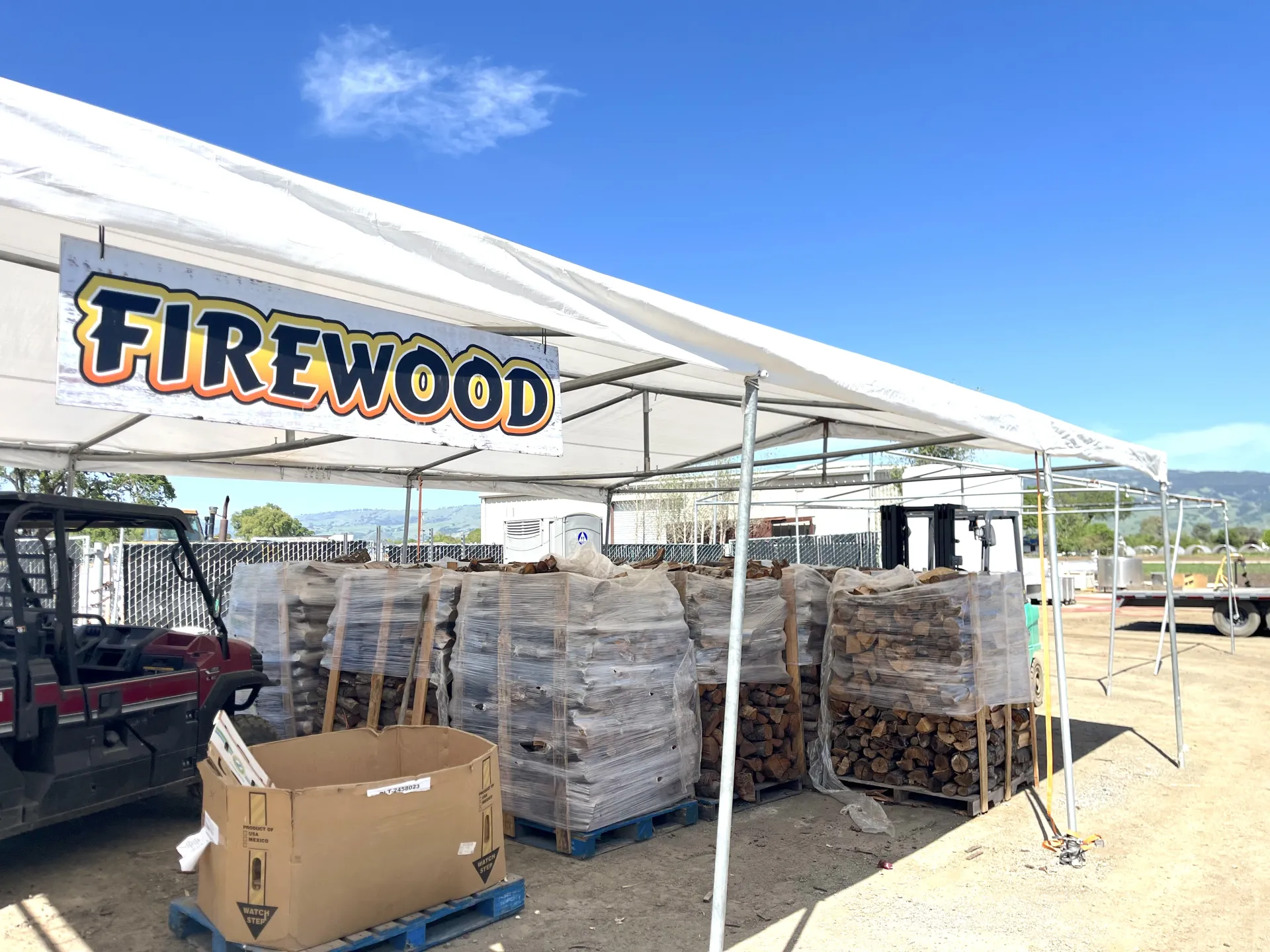 Stacks of firewood for sale below a canopy with a sign that says "firewood."