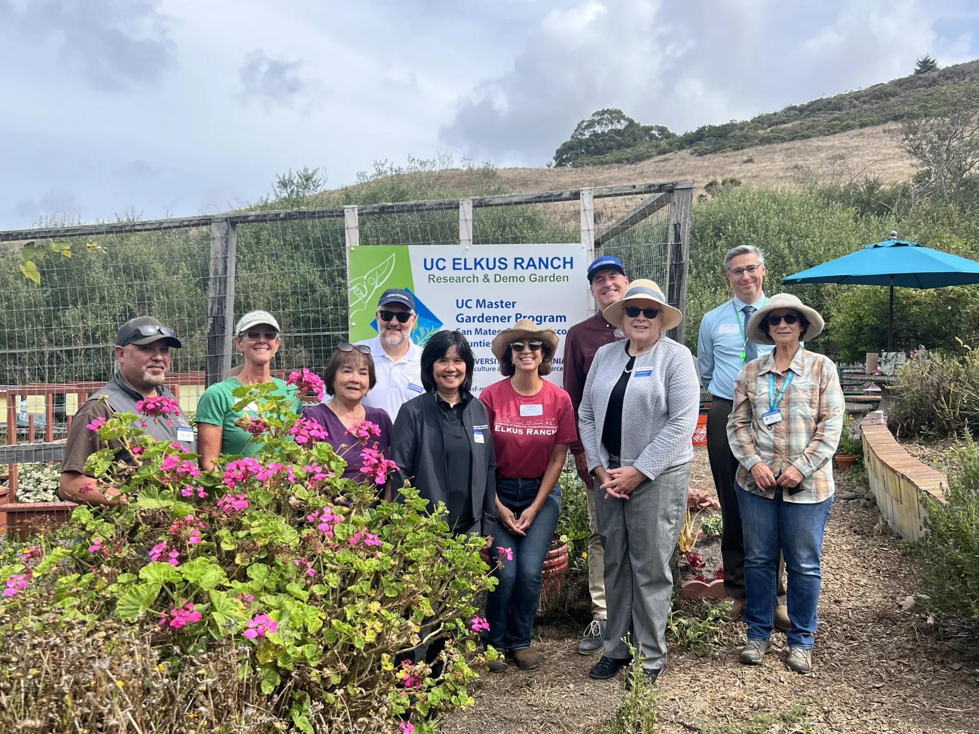 A group of 10 people pose beside a flowering pink geranium bush at UC Elkus Ranch