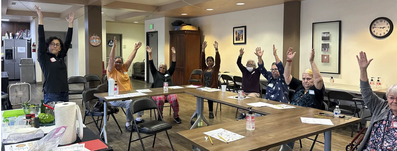 Residentes mayores de Oaks on Florence realizan ejercicios de estiramiento como parte de una clase de nutrición y bienestar impartida por CalFresh Healthy Living, UCCE Los Ángeles. La iniciativa promueve hábitos saludables a través de actividades prácticas y educación culturalmente relevante.