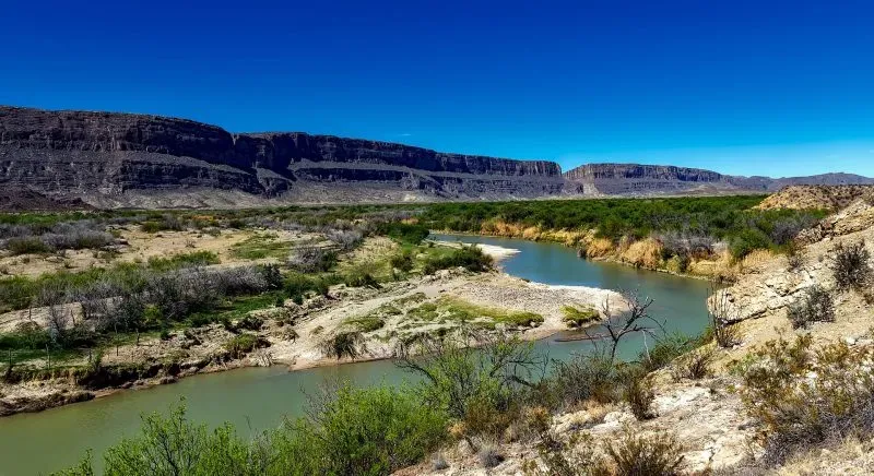 The Rio Grande River winds through a desert landscape with green shrubs