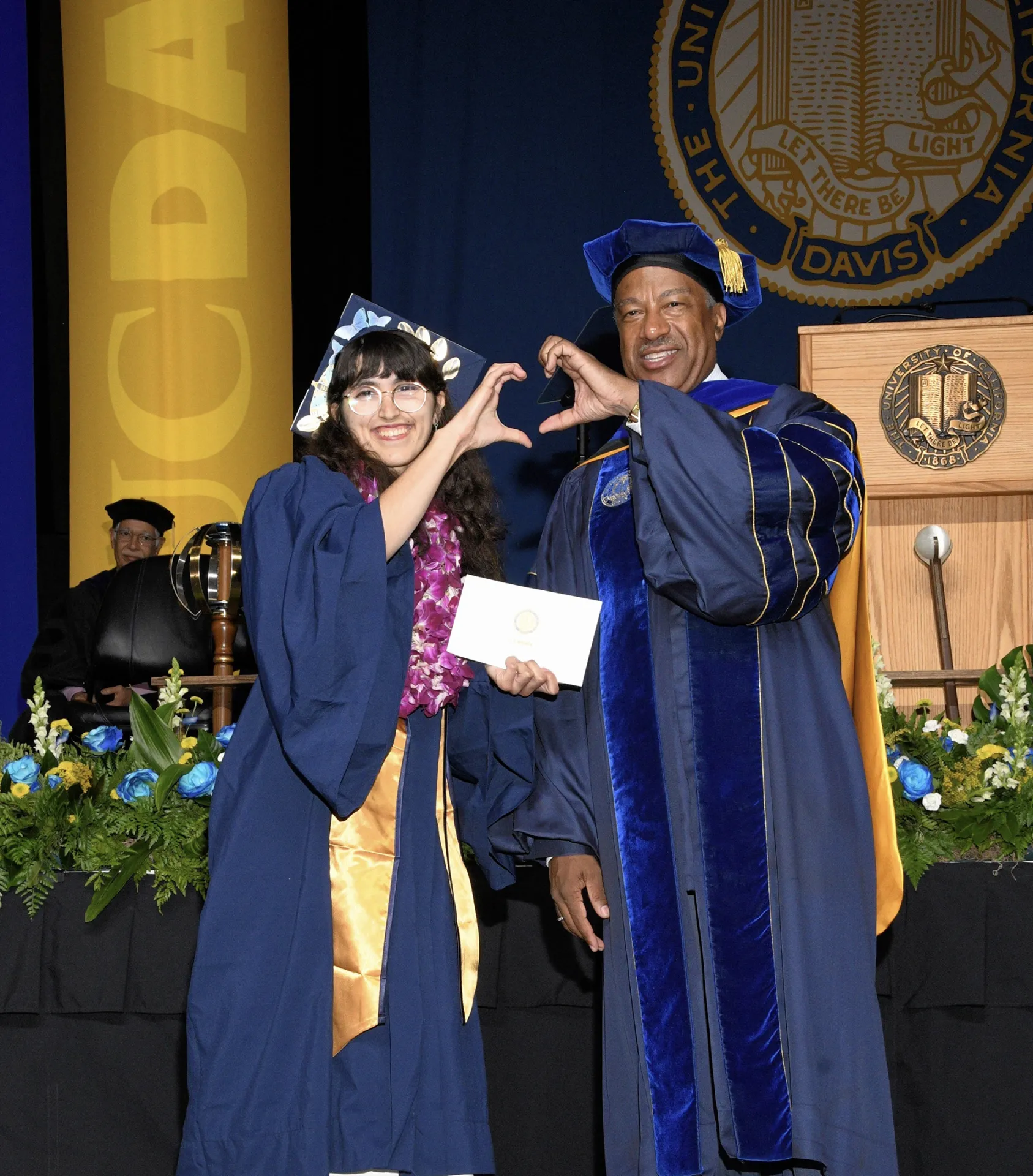 Samantha Murray of the UC Davis Class of 2025 forms a heart with UC Davis Chancellor Gary May.