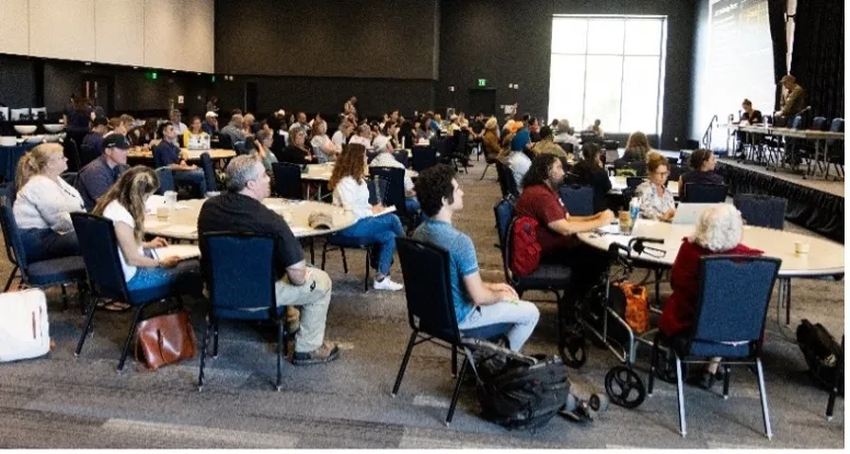 People sit in chairs at round tables facing the stage