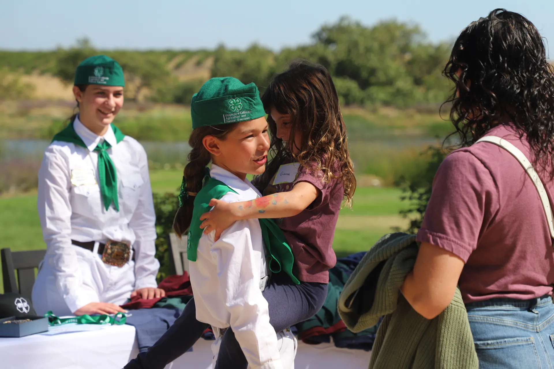 A girl in a 4-H uniform carries a younger girl.