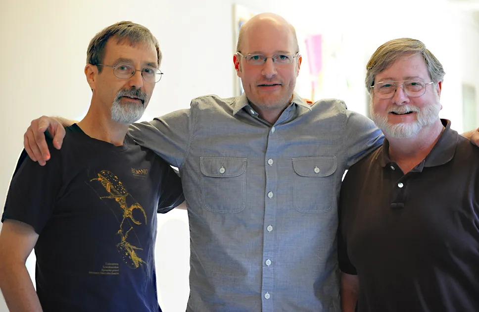 Three men standing with arms over shoulders of those next to them