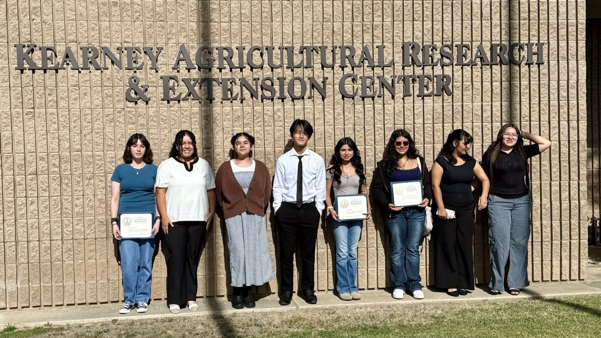 Eight students stand under the Kearney Agricultural Research and Extension Center sign