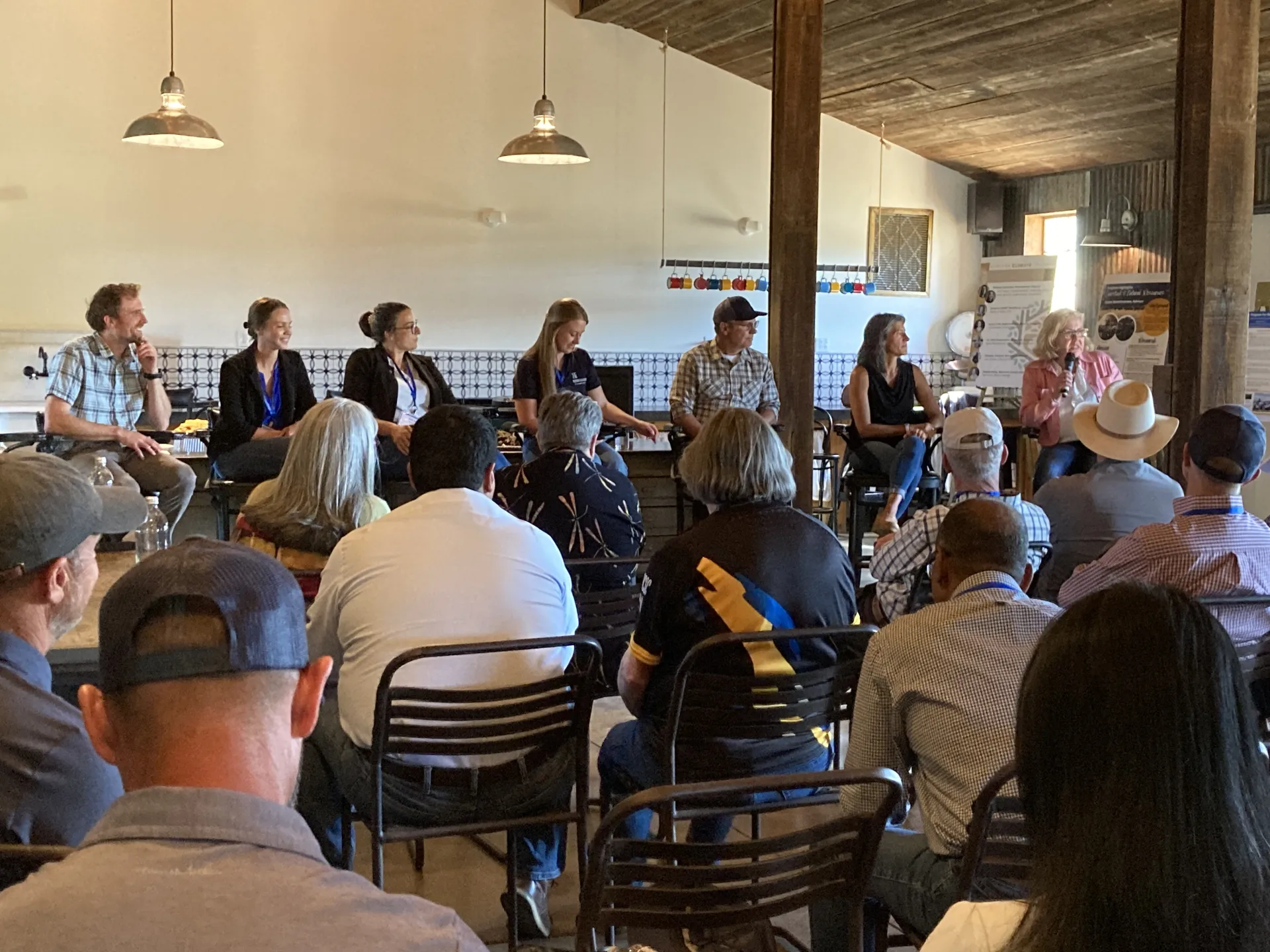 Seven people sit on tall chairs facing the audience