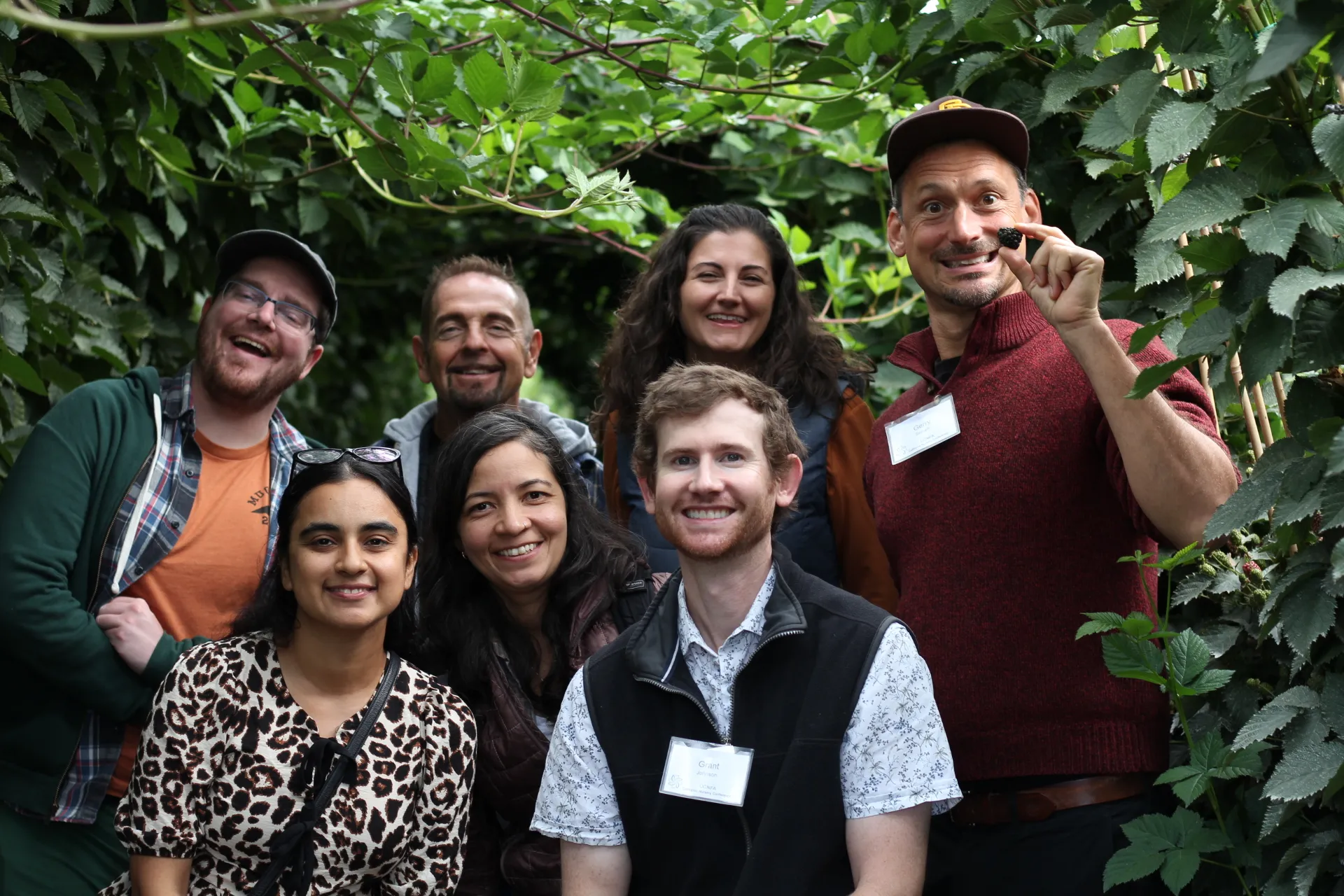 A group of smiling people gathered between berry vines.