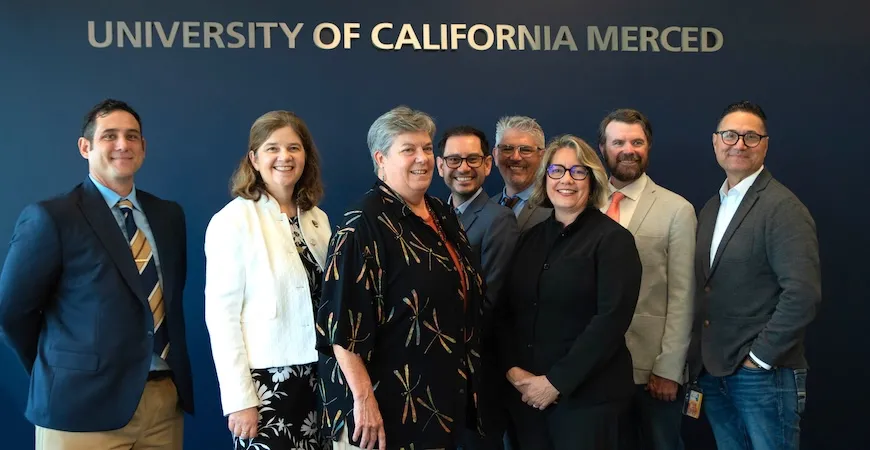 Eight people stand under a sign: University of California Merced