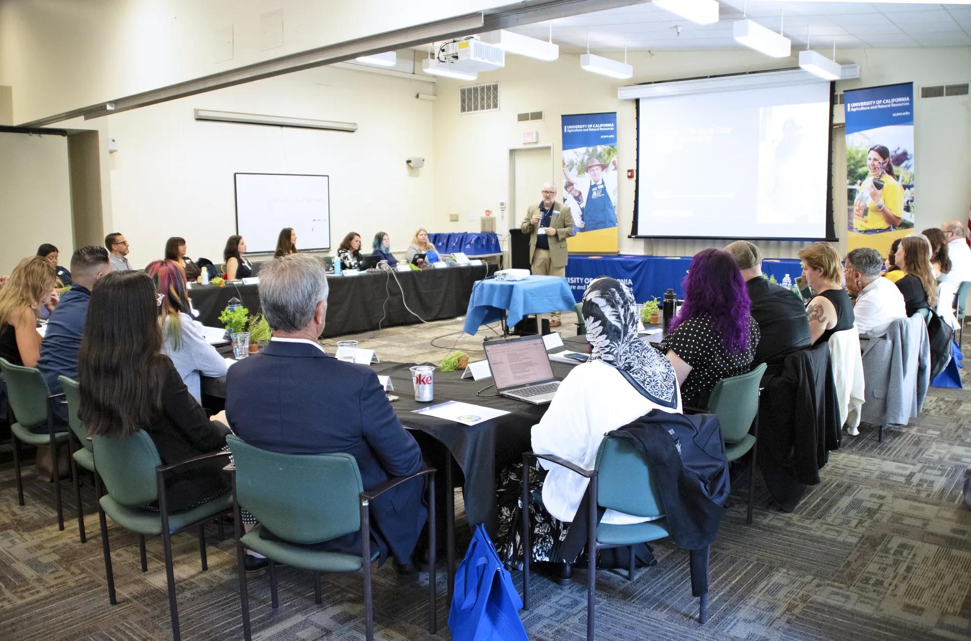 Brent speaks to group sitting at tables in horseshoe formation
