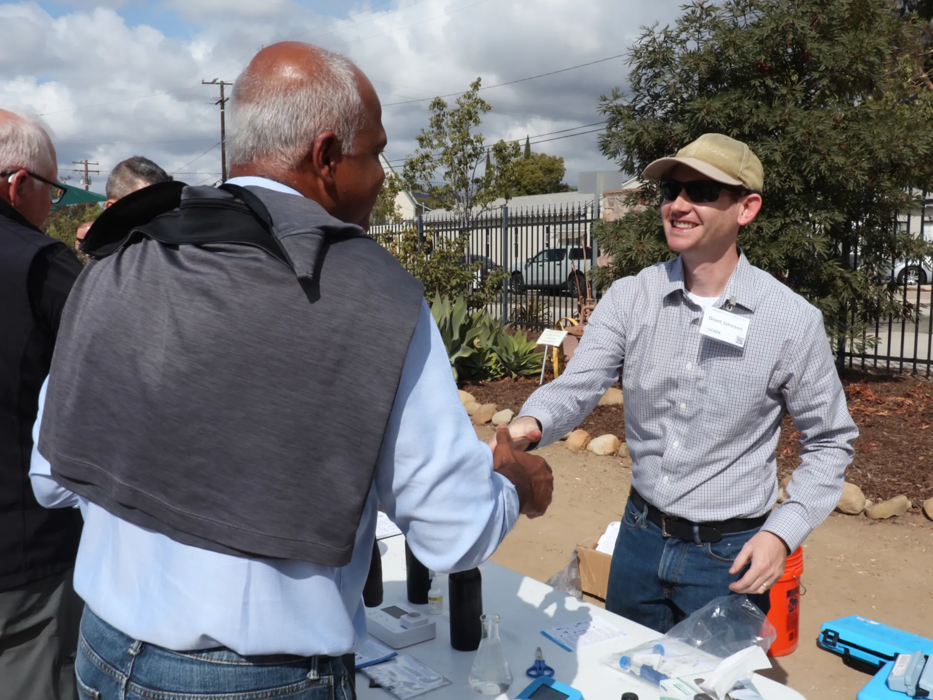Two people shake hands over a table outside