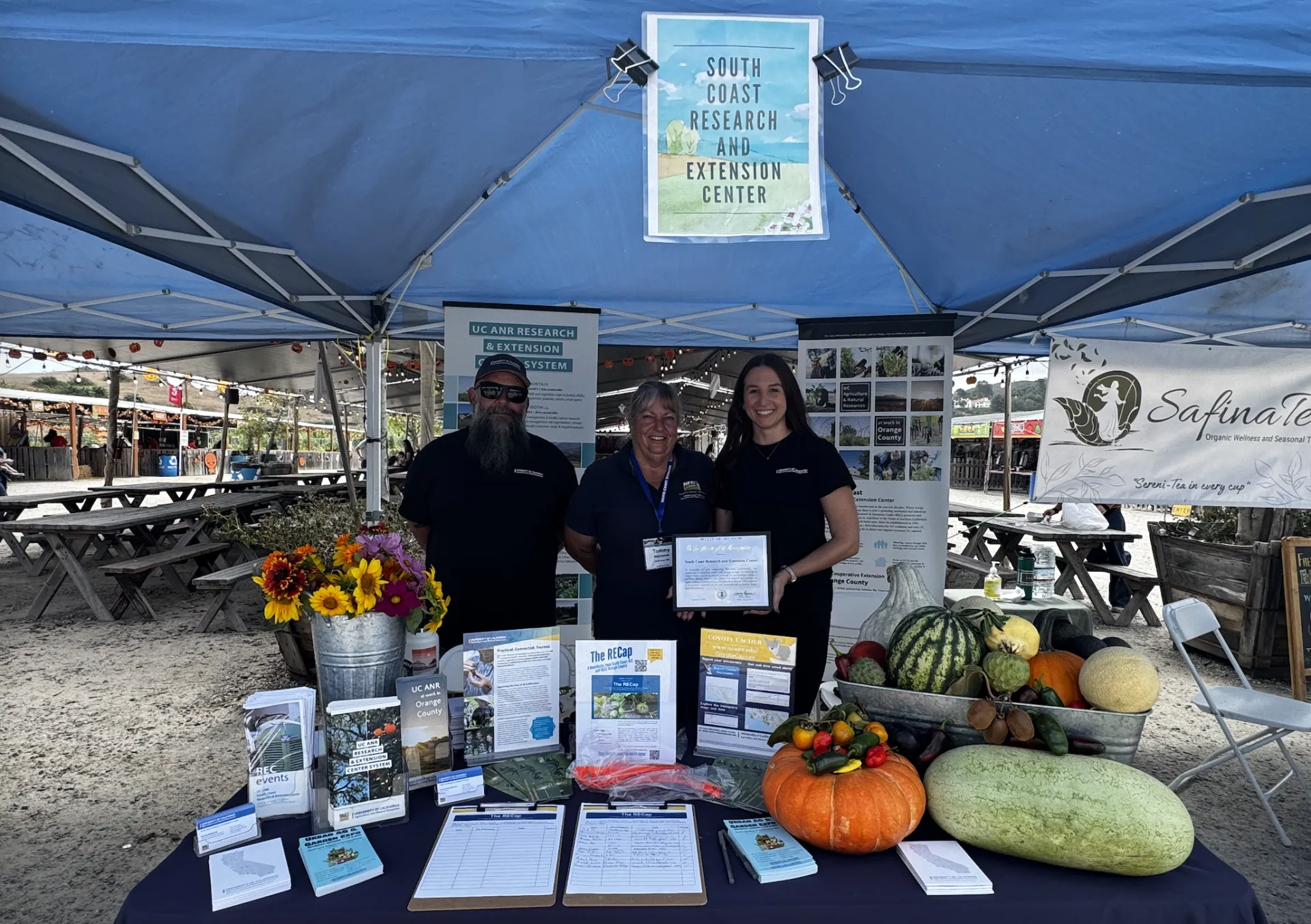 Three people stand under a tent behind a display table