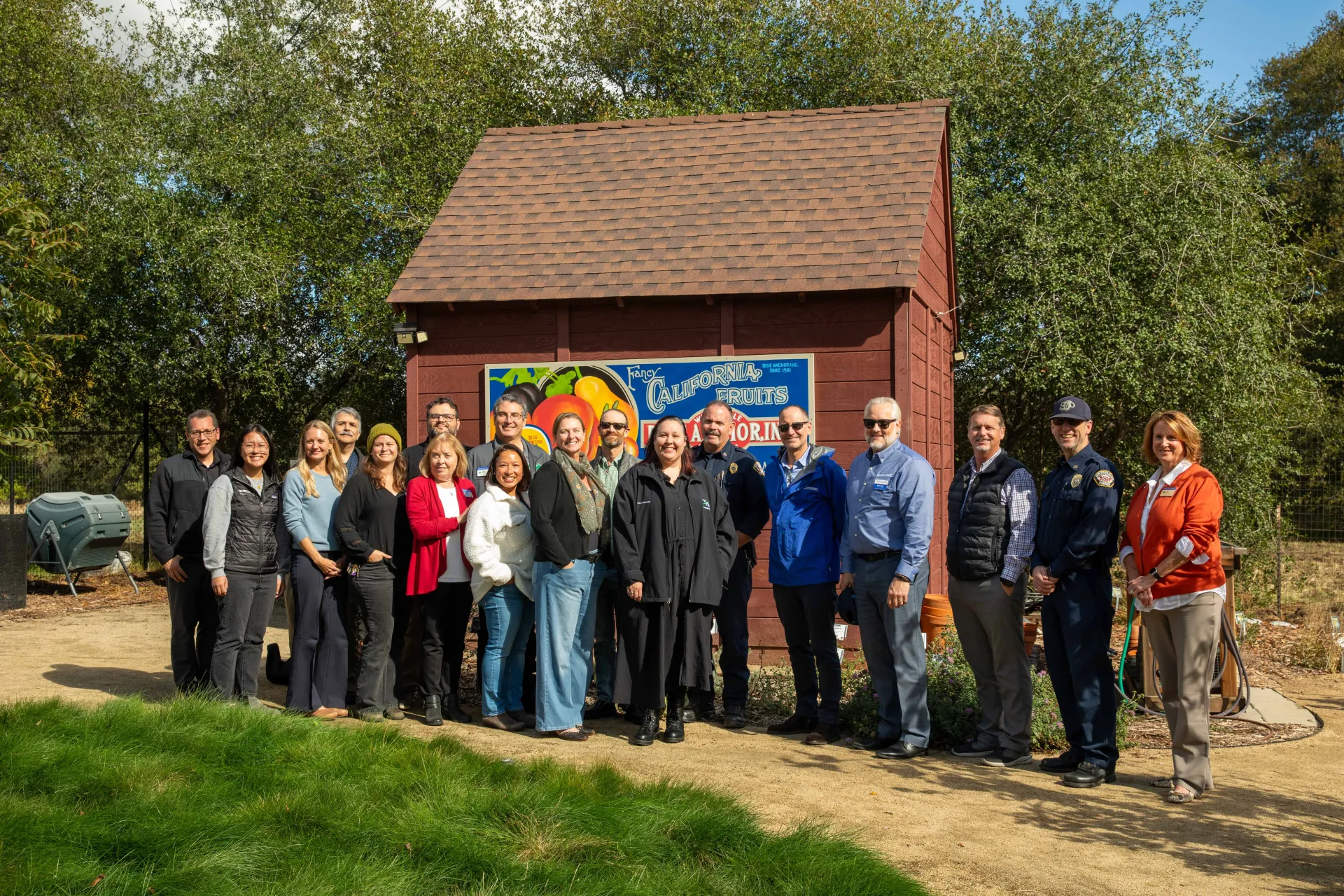 18 people pose in front of a shed with sign: California Fruits