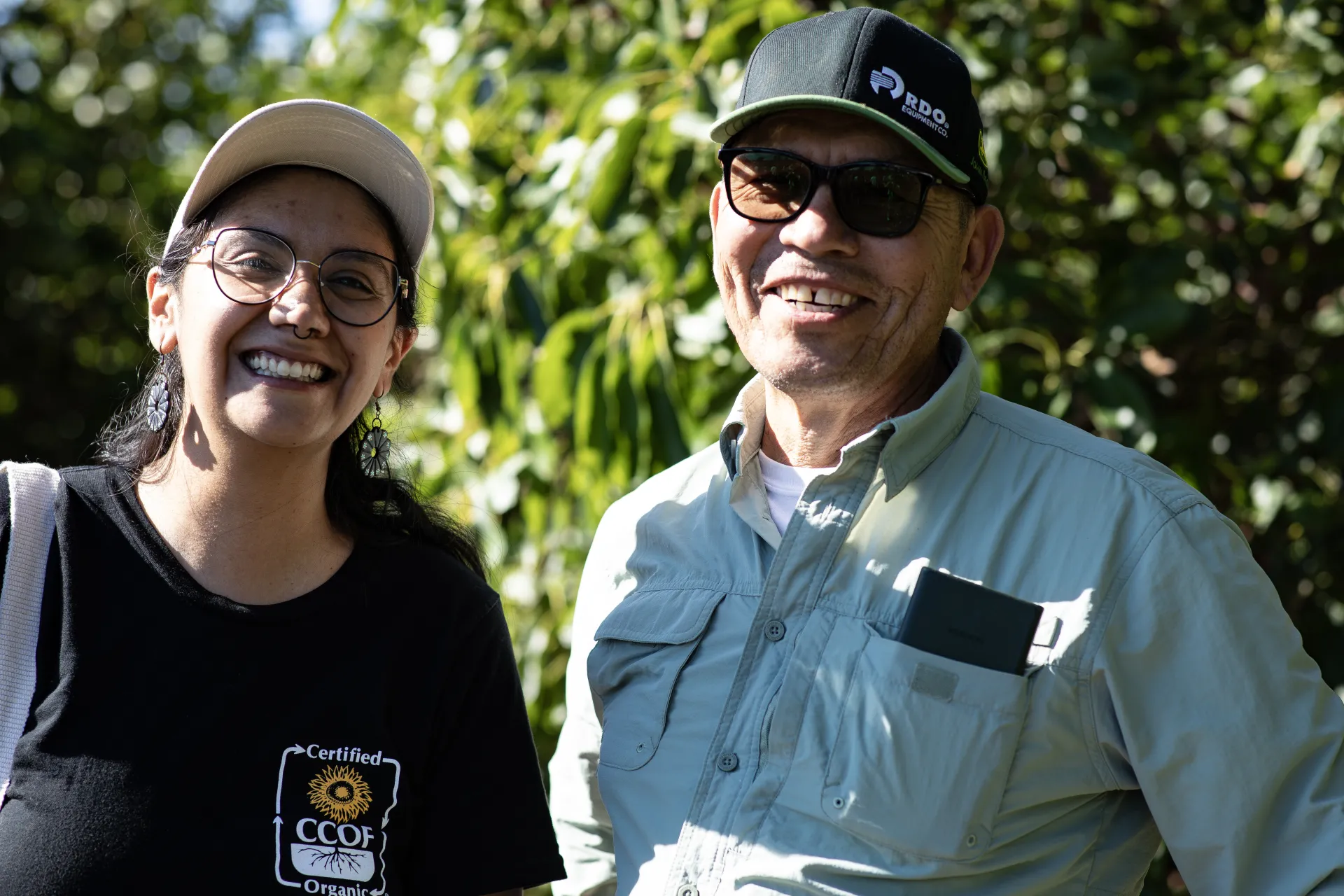 Two people wearing hats stand in an orchard