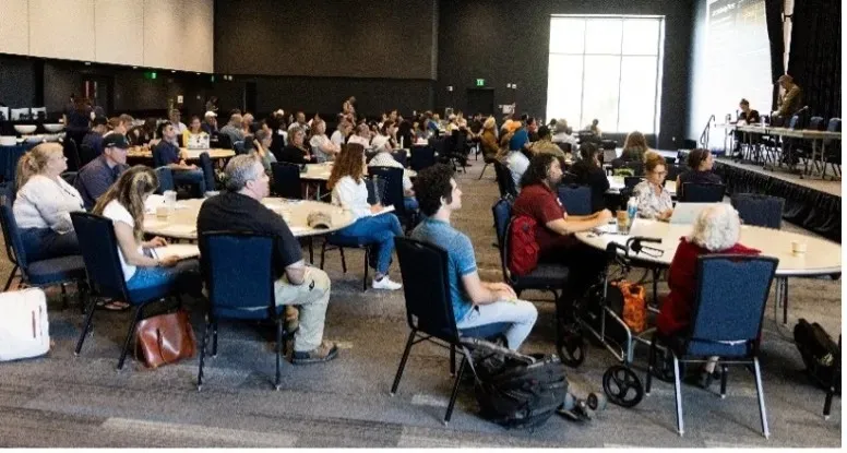 Personas sentadas alrededor de mesas escuchan a los presentadores.